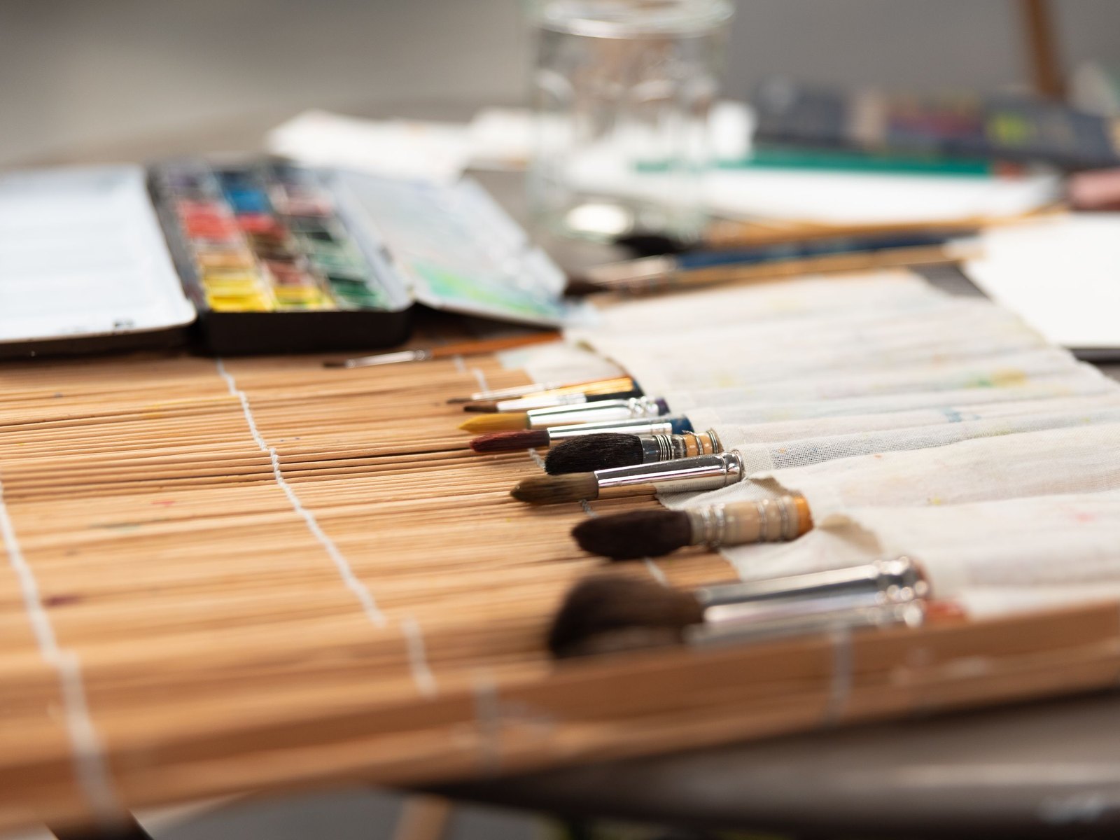 机に広げた布のケースに、太さのちがう絵筆が何本も並び、奥に絵の具のセットが置かれている
