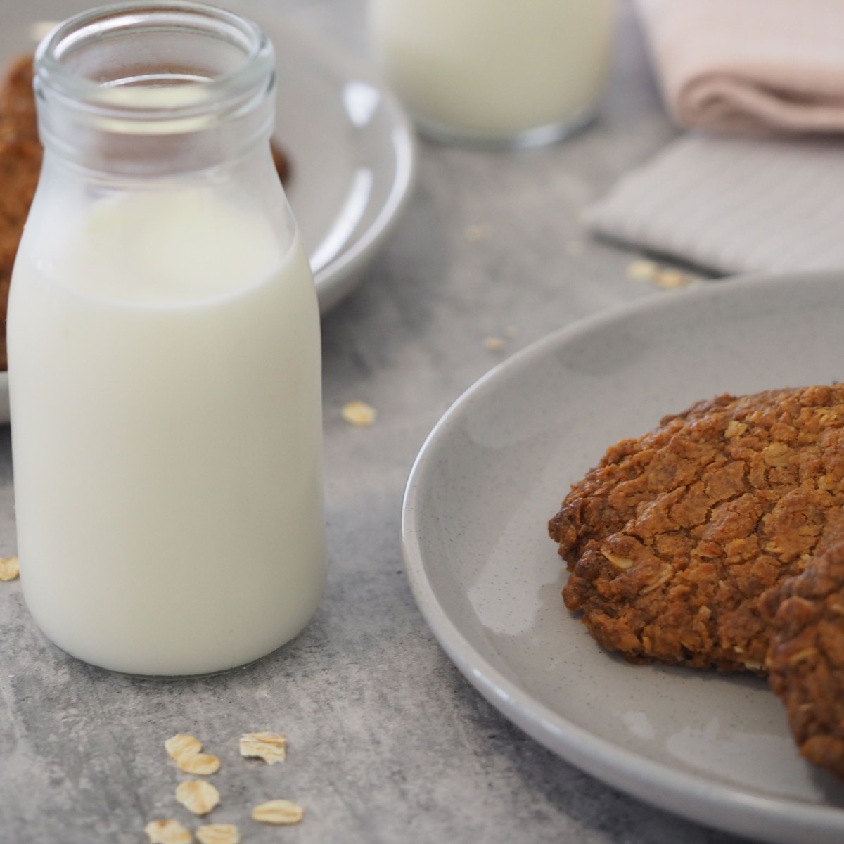 テーブルに置かれた牛乳のびんと、白い皿にのったオートミールのクッキー