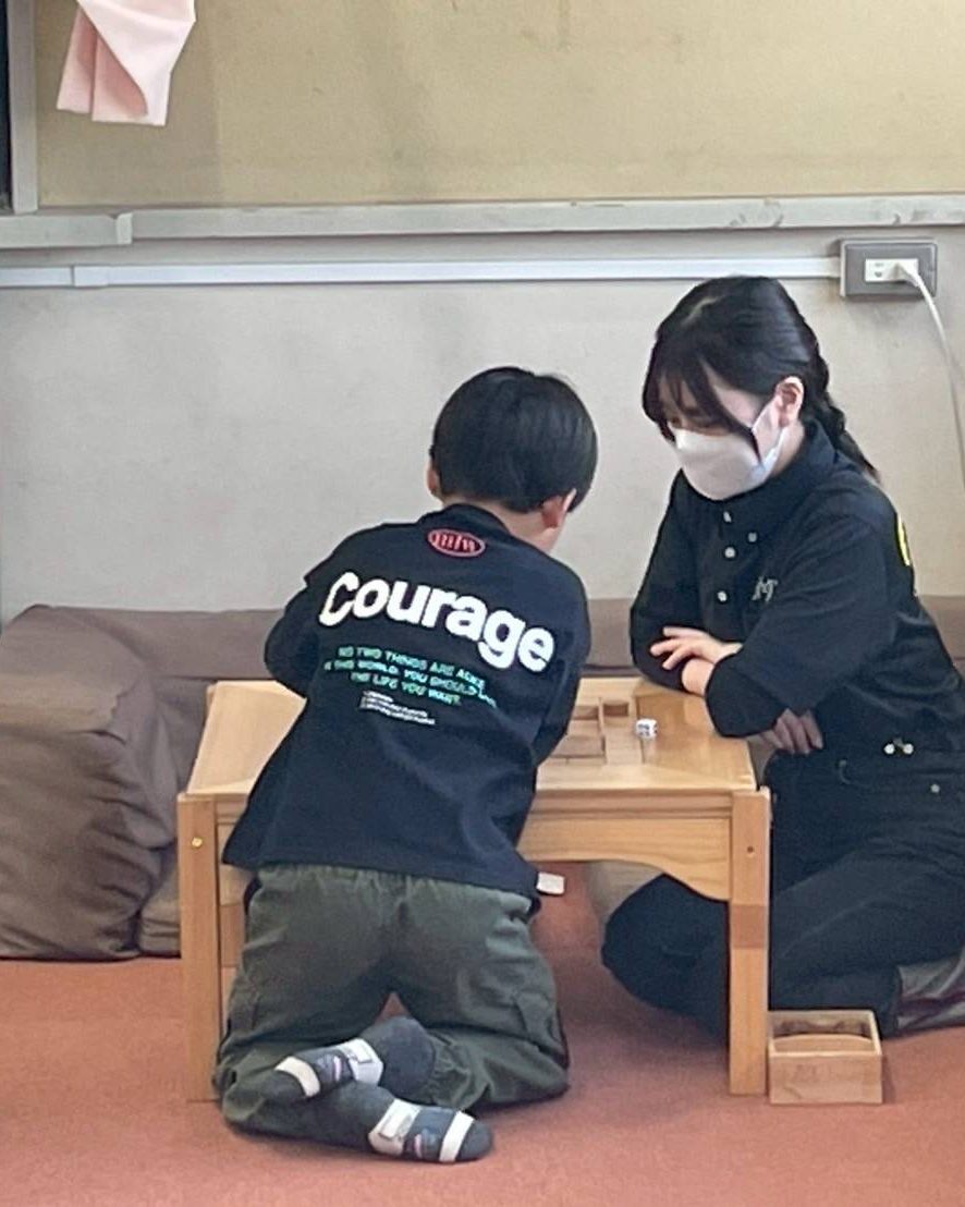 低い木の机をはさんで、支援員と子どもが向かい合って積み木で遊んでいる