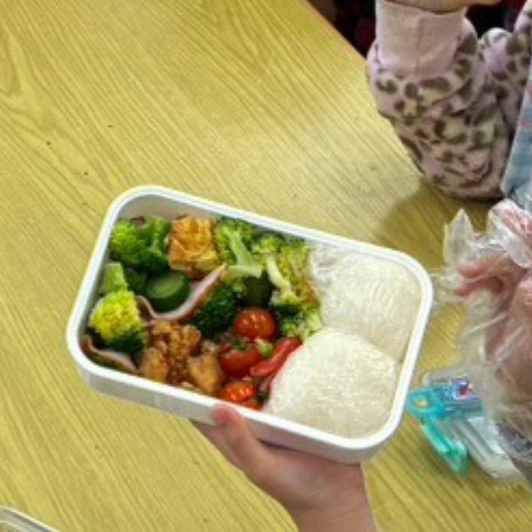 お弁当箱を両手で持つ子どもの手元。ごはんとおかずが詰まっている