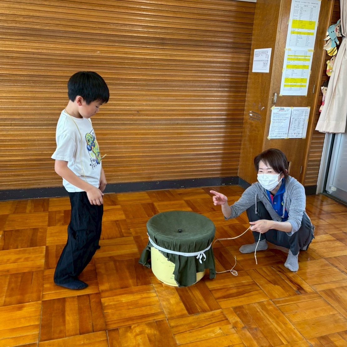 板張りの部屋で、支援員と子どもがコマ回しをしている